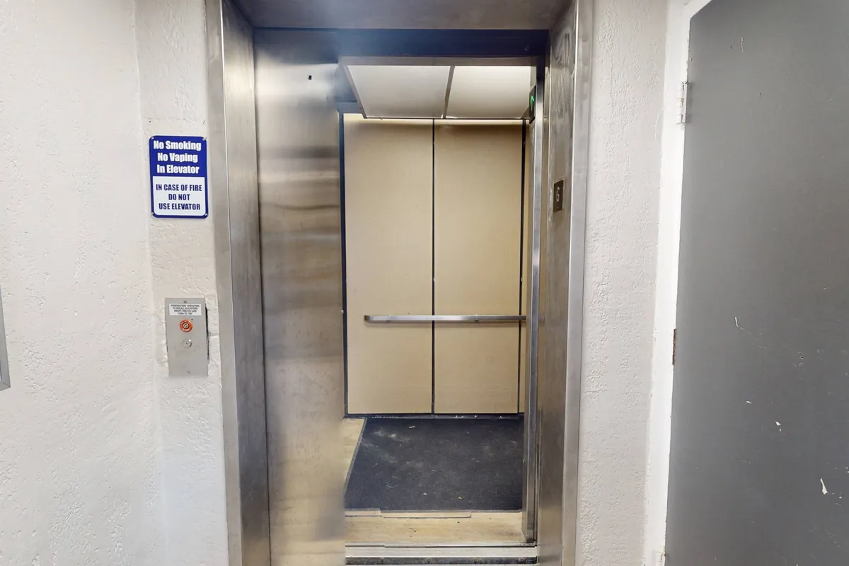 A modern elevator lobby with stainless steel elevator doors, illuminated buttons, and a visible safety sign, conveying the accessibility and comfort of moving between floors.