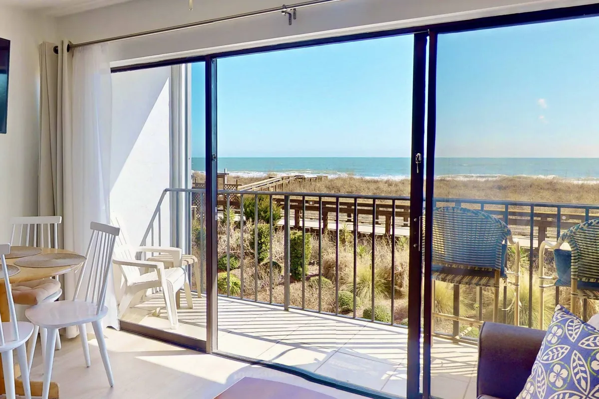 A bright and welcoming clubhouse lounge area with large glass sliding doors offering an ocean view, comfortable patio furniture, and a peaceful ambiance—ideal for reading, socializing, or unwinding.