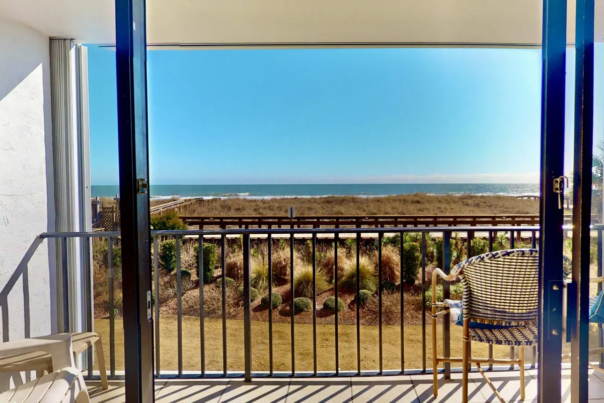 This image offers a serene view from a private balcony overlooking the ocean, with a lounge chair inviting relaxation and a landscaped garden below. The clear sightlines to the water and the gentle ambiance suggest a tranquil and romantic setting ideal for quiet mornings or evenings.