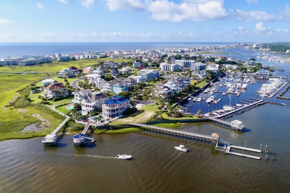 A relaxed waterfront scene showcasing marina-front residences, boats moored at the docks, and green spaces along the shoreline. The setting sun casts a warm glow over the entire area, emphasizing both the natural scenery and vibrant community life.