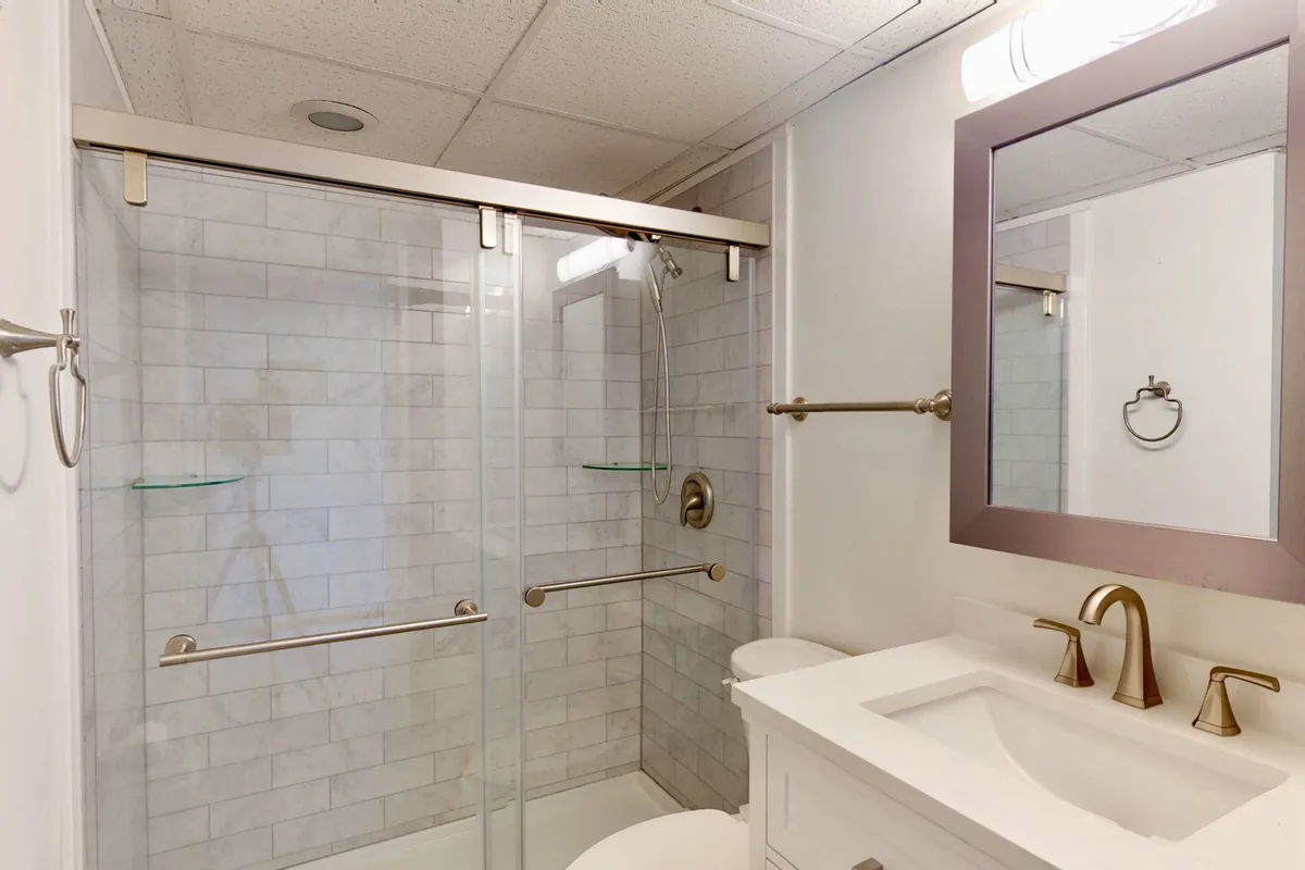 A modern en-suite bathroom featuring a glass shower enclosure, sleek vanity with a sink, and a large mirror. The space feels refreshing and serene, inviting guests to unwind and rejuvenate after a sun-filled day.